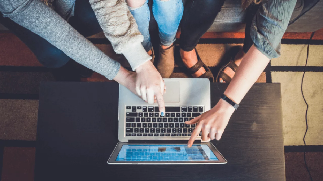 two people pointing at newsletter on laptop