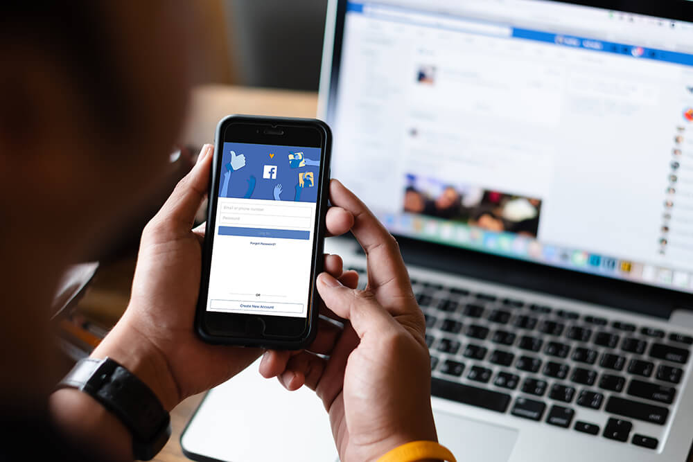 A person using Facebook on both smartphone and laptop