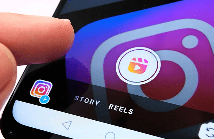 Close-up of a finger tapping a smartphone screen displaying the Instagram camera interface with the Reels icon selected