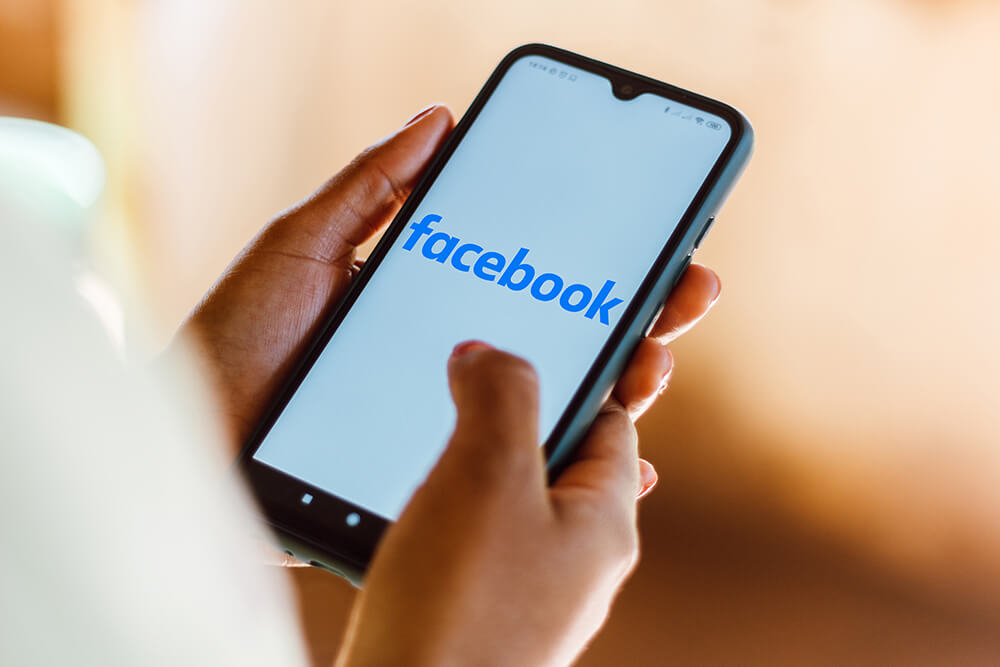 Smartphone, held by a person, displaying the Facebook logo