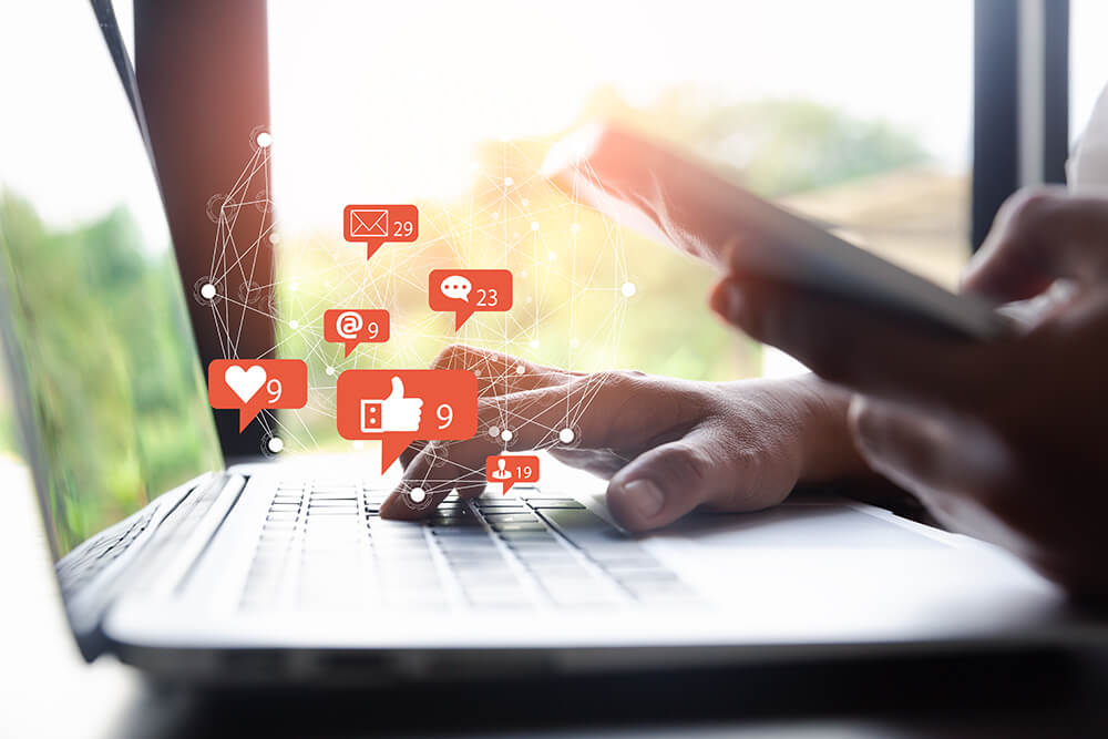 Hands typing on a laptop with floating social notification icons and counts