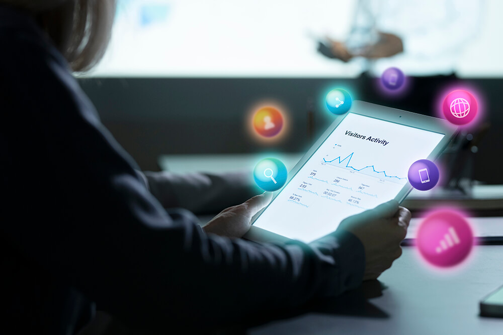 Person holding a tablet with a visitor analytics graph and floating digital app icons